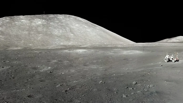 Monochrome lunar landscape with a large hill and a small rover with astronauts on the right.