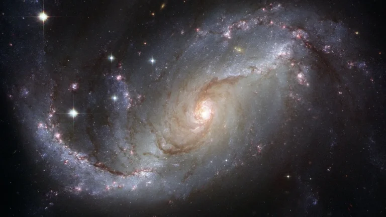 A vibrant barred spiral galaxy displays intricate dust lanes and brilliant star clusters against a dark cosmic background.