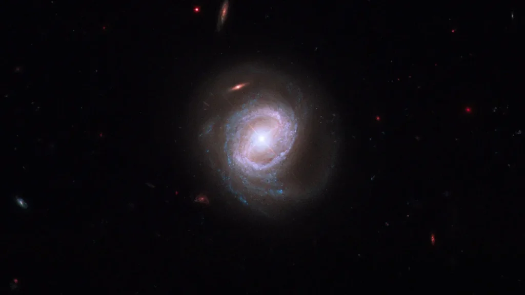 A brilliant spiral galaxy with glowing blue arms and a bright central core shines in the dark cosmos.