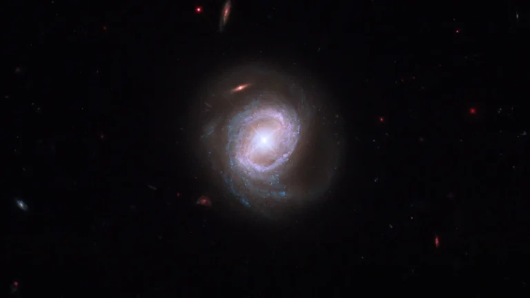 A brilliant spiral galaxy with glowing blue arms and a bright central core shines in the dark cosmos.