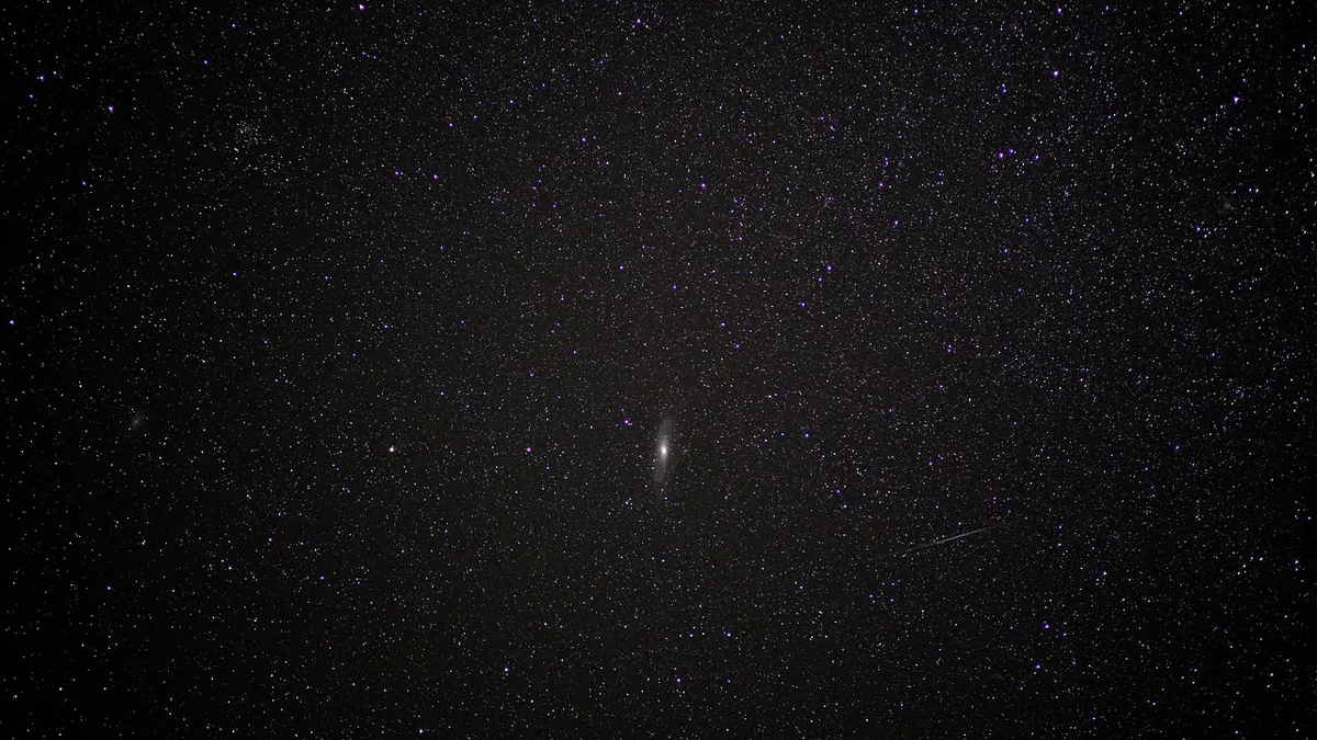 A wide-field view of a starry night sky with a central galaxy, representing deep space.