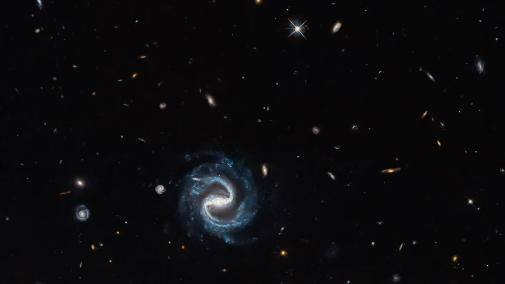 A bright blue spiral galaxy spins in a deep field of distant galaxies and stars.