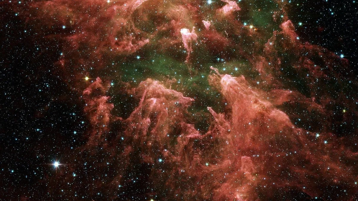 A vibrant cosmic landscape of the Cat's Head Nebula, showing red dust clouds and a field of bright stars.