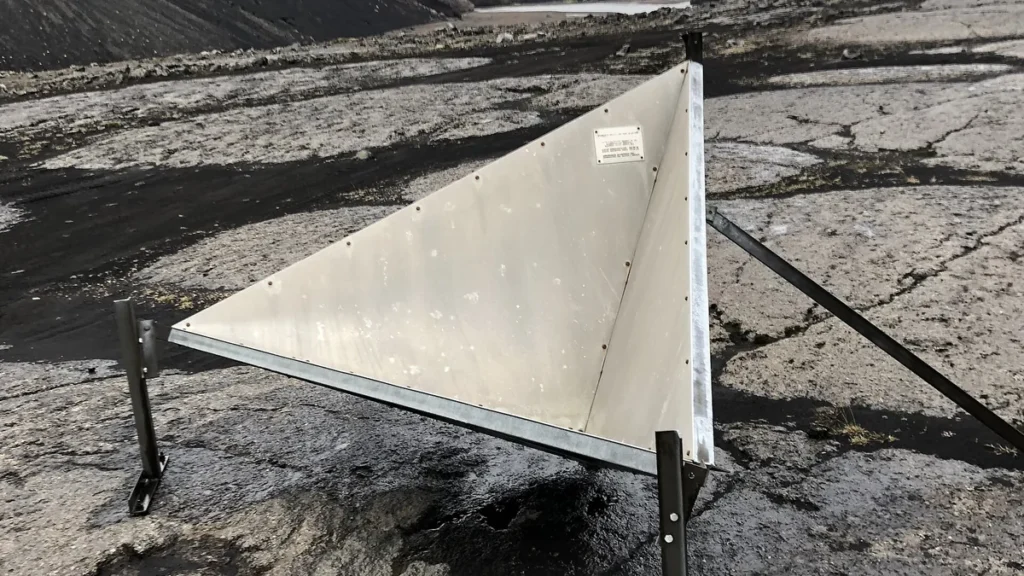 A trihedral corner reflector on a dark, rocky landscape used for SAR satellite calibration.