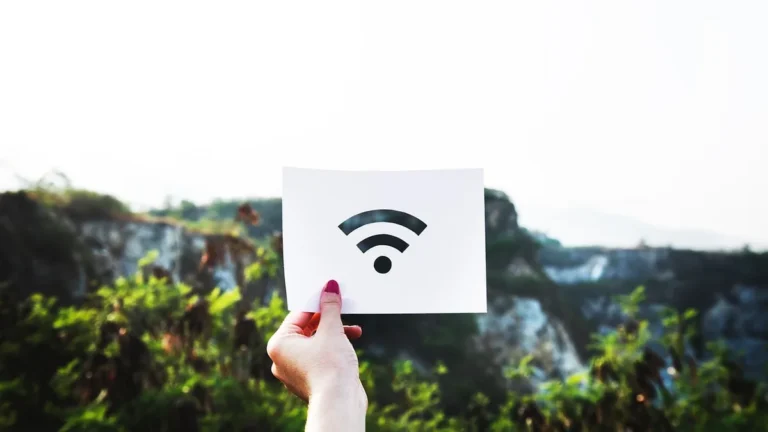 A hand holding a white sheet of paper with a black Wi-Fi symbol against a blurred green landscape background.