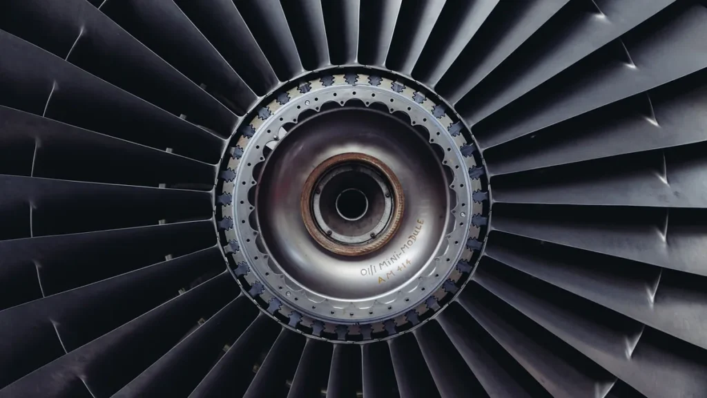 A close-up, symmetrical view of a dark metallic jet engine turbine with a silver central hub.
