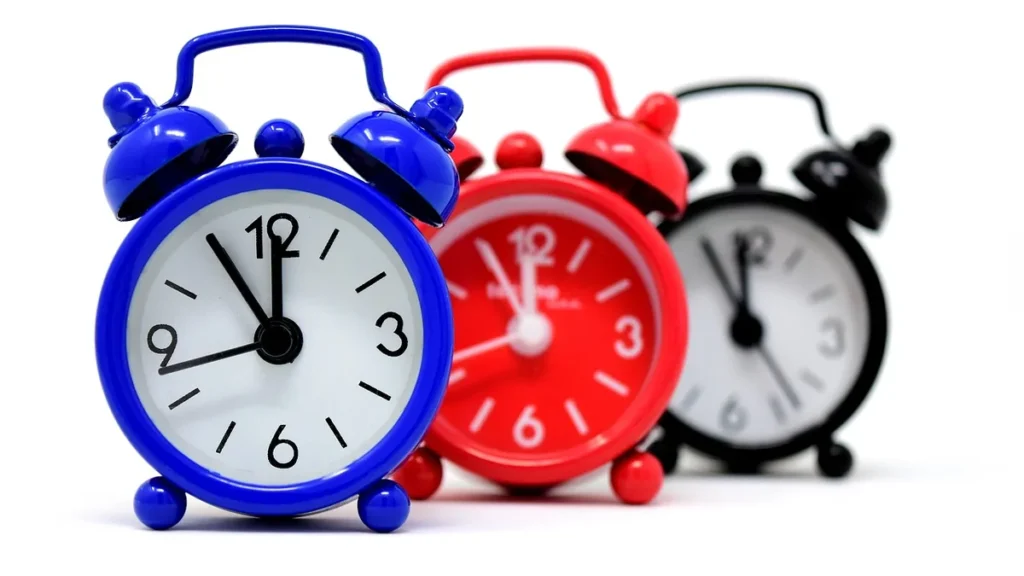 Three colorful alarm clocks in blue, red, and black lined up on a white background.