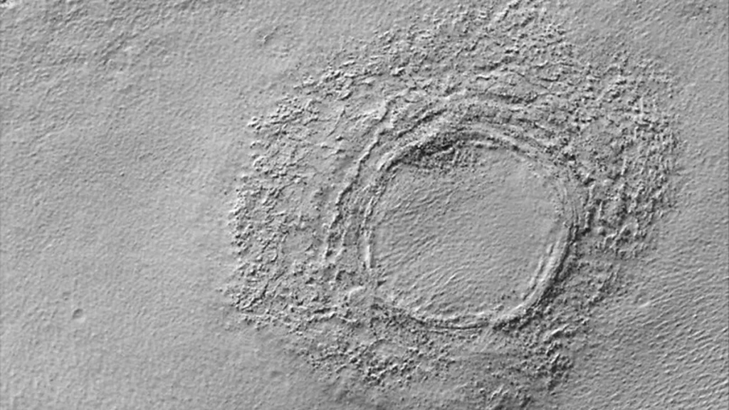 A black-and-white close-up of a circular crater surrounded by rough, dusty terrain on a planetary surface.