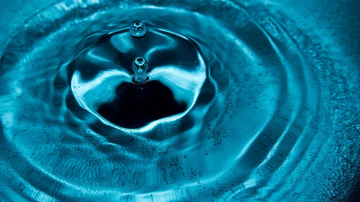 Abstract close-up of vibrant blue water ripples and droplets forming concentric circular patterns.