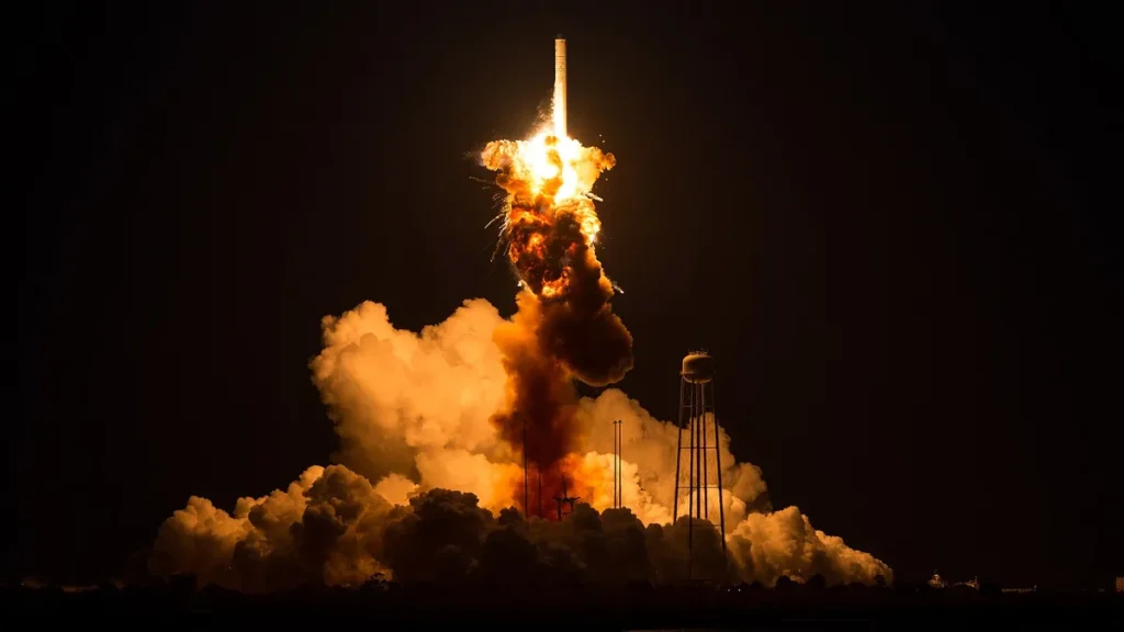A rocket explodes in a bright orange fireball during a night launch, with thick clouds of smoke billowing below.