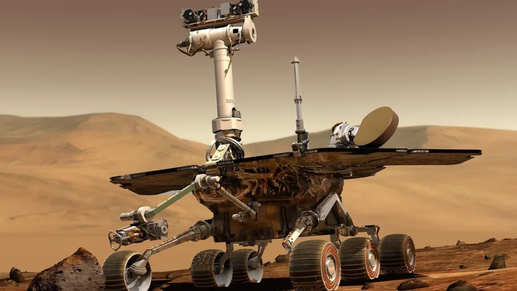 A robotic Mars rover stands on the red, dusty Martian surface against a backdrop of rolling hills under a hazy orange sky.