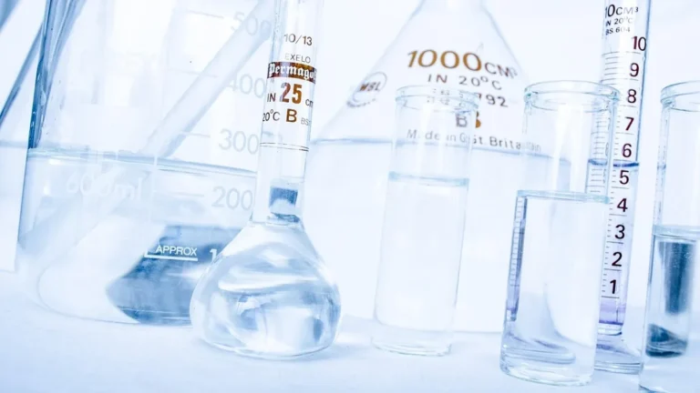 Laboratory glassware including beakers, flasks, and graduated cylinders filled with clear blue-tinted liquid.