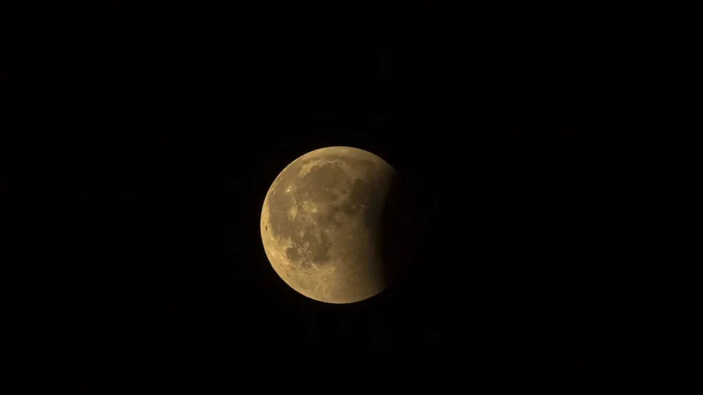 A golden-orange moon partially shadowed by a lunar eclipse against a dark black sky.