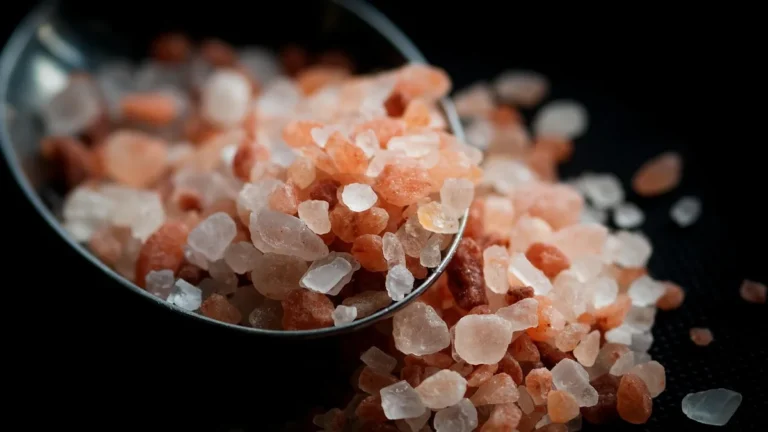 Coarse pink salt crystals on a spoon spilling onto a dark surface.
