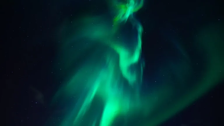 Vibrant green aurora borealis dancing across a star-filled dark night sky.