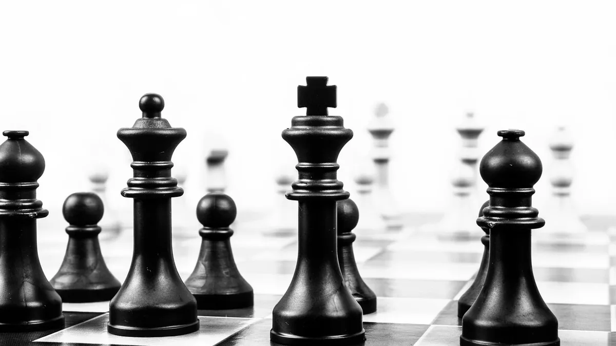 Black king chess piece stands prominently on a chessboard in a high-contrast black and white photo.