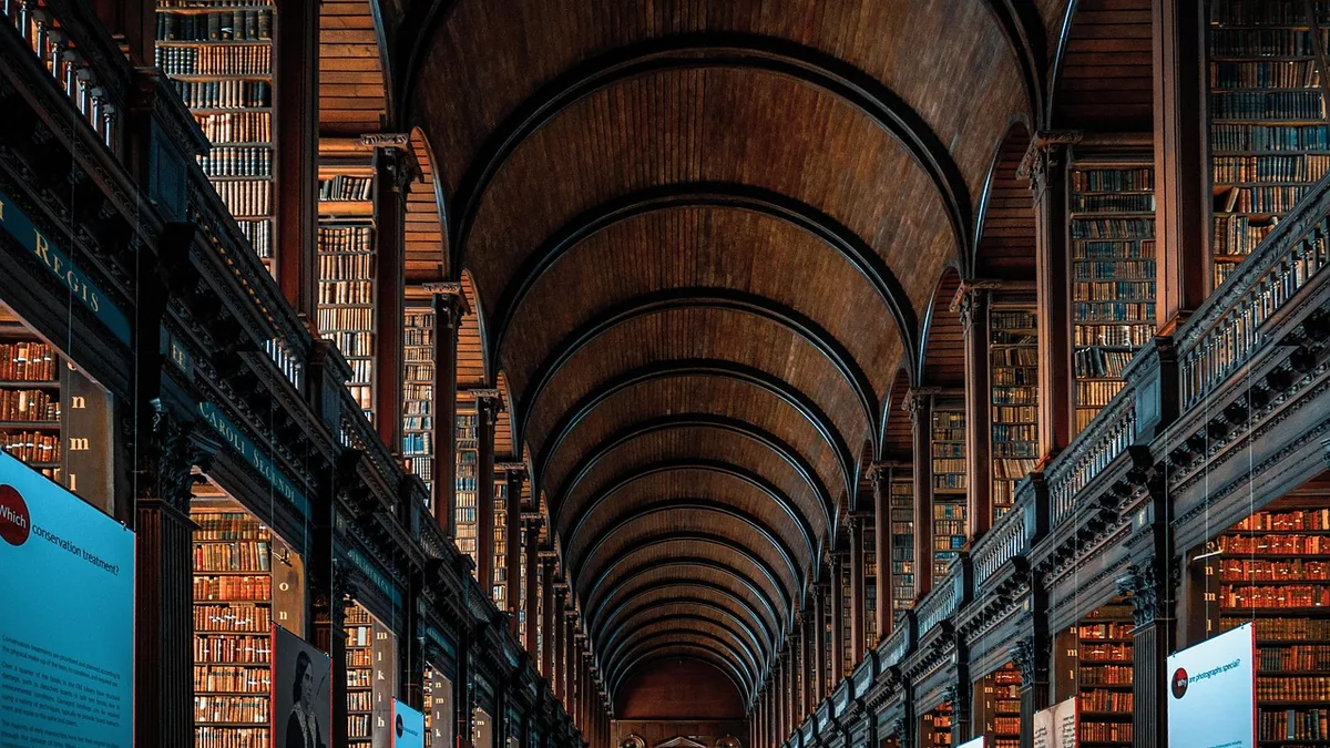 Grand historic library corridor with arched wooden ceiling and towering bookshelves stretching into the distance.