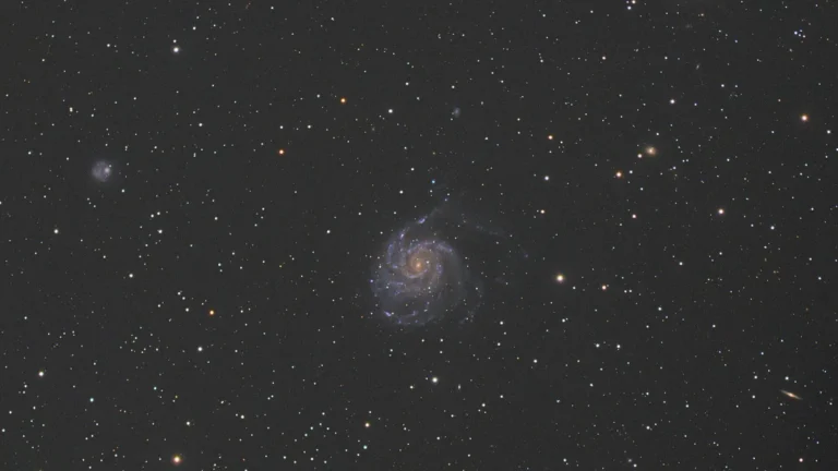 A spiral galaxy with prominent arms surrounded by a field of stars and distant galaxies.