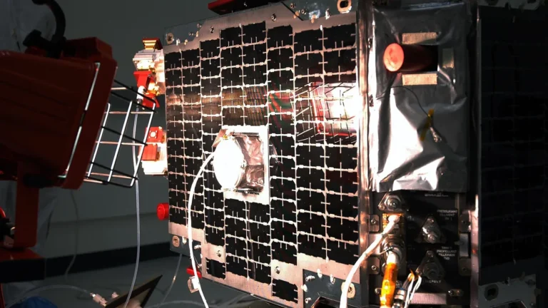 Close-up of a satellite's solar panels and propellant system hardware in a cleanroom environment.