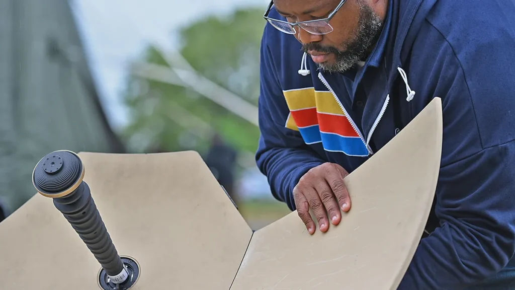 A close-up of a technician inspecting a beige, angular satellite dish, likely part of a Starlink setup.
