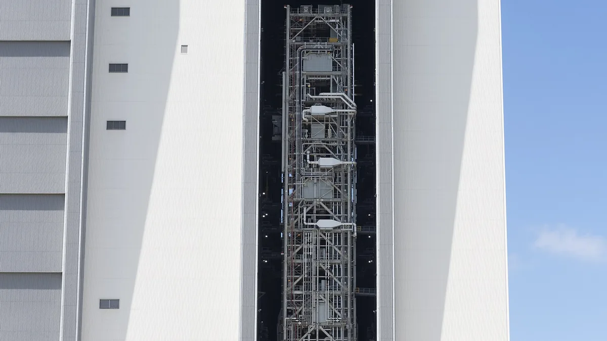 Vertical view of the massive white VAB building showing complex metal scaffolding inside a dark high bay opening.
