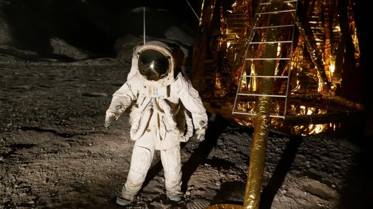 Astronaut in a white spacesuit stands on lunar soil next to a golden lander with a ladder.
