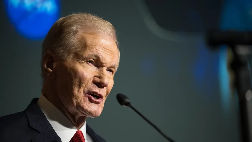 Close-up of NASA Administrator Bill Nelson speaking at a microphone with a blurred blue NASA logo behind him.