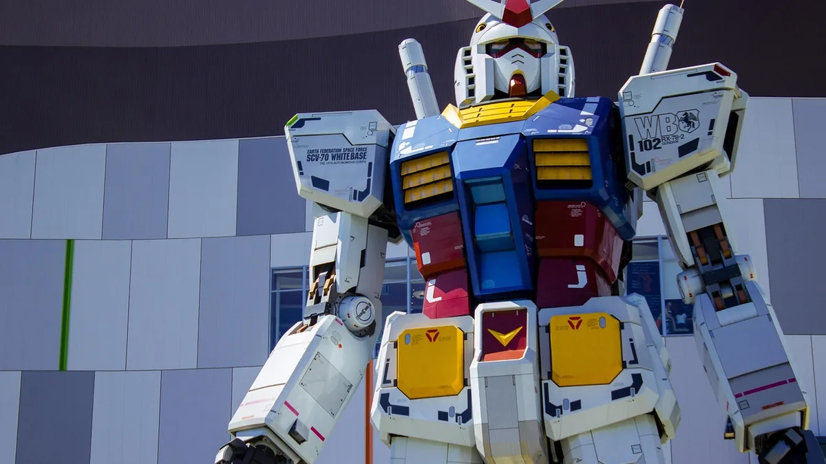 Close-up of a giant, colorful RX-78-2 Gundam robot statue against a modern paneled building.