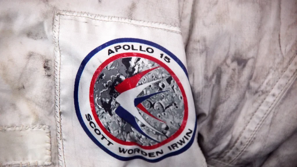 Apollo 15 mission patch with crew names Scott, Worden, Irwin on a dusty white spacesuit.