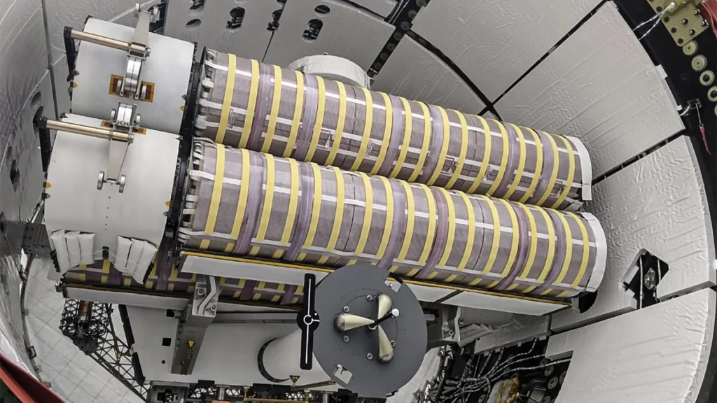 Cylindrical roll-out solar arrays bundled with yellow straps inside a spacecraft payload container.