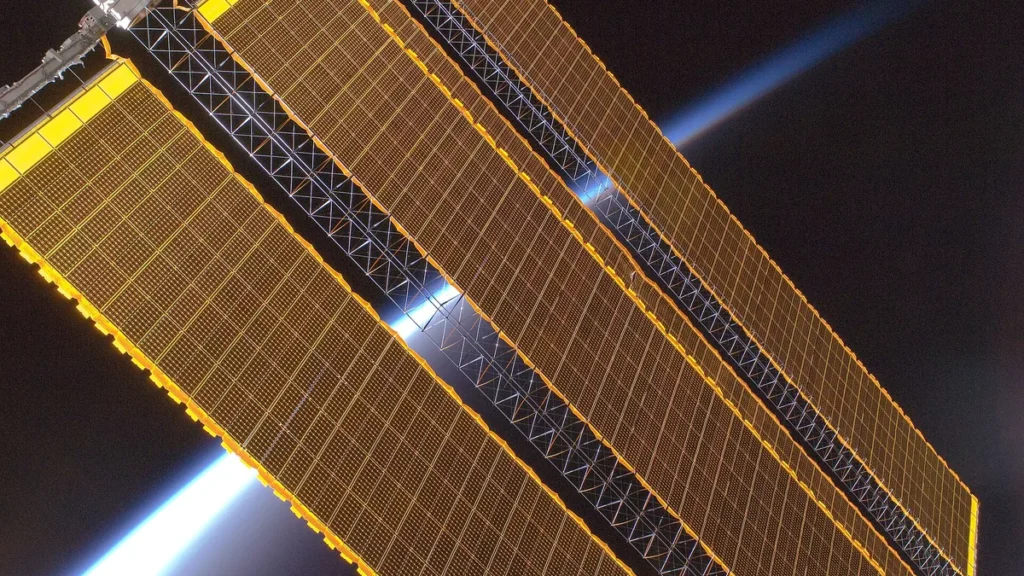 Golden solar panels stretch across a space station truss with Earth's bright blue limb glowing in dark space.