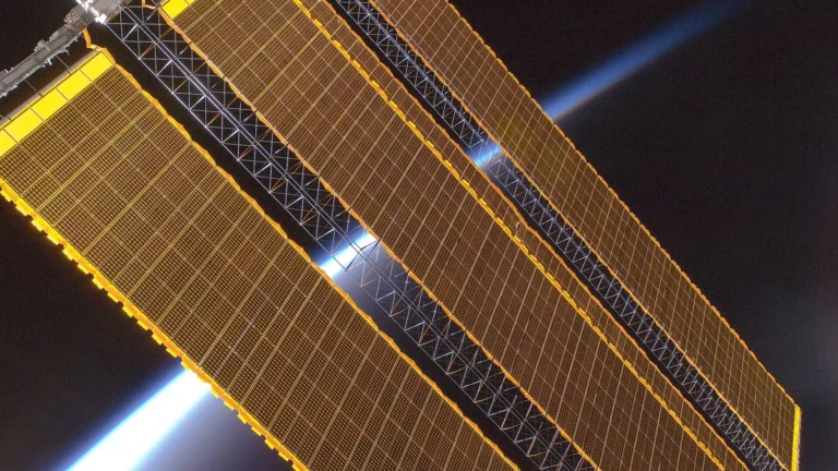 Golden solar panels stretch across a space station truss with Earth's bright blue limb glowing in dark space.