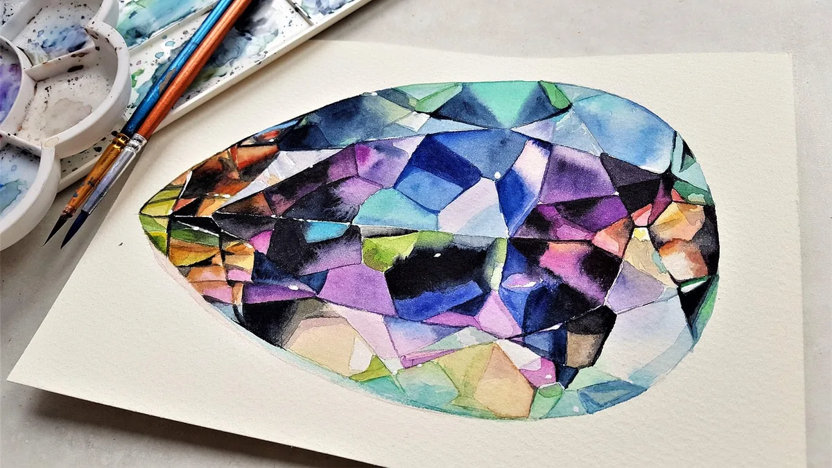 Vibrant watercolor painting of a multicolored faceted crystal gemstone on paper with paintbrushes and palette nearby.