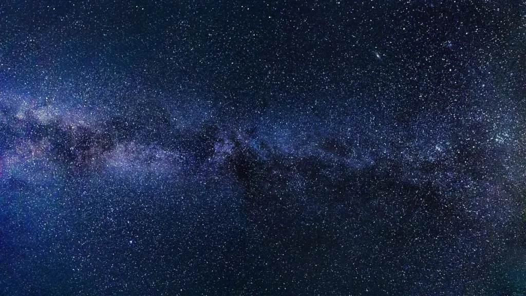 A starry night sky with the colorful purple and blue band of the Milky Way stretching across the cosmos.