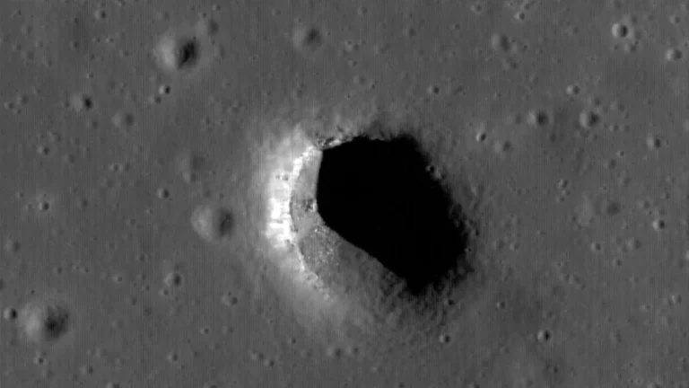 A black-and-white view of a deep, shadowed lunar pit surrounded by cratered terrain.