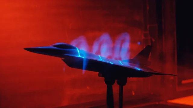 A jet model in a red-lit wind tunnel with blue glowing lines visualizing airflow vortices.