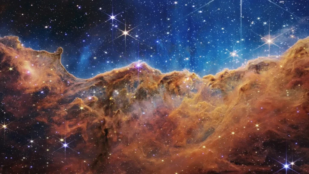 A vibrant cosmic landscape of orange nebula clouds silhouetted against a bright blue starry sky.