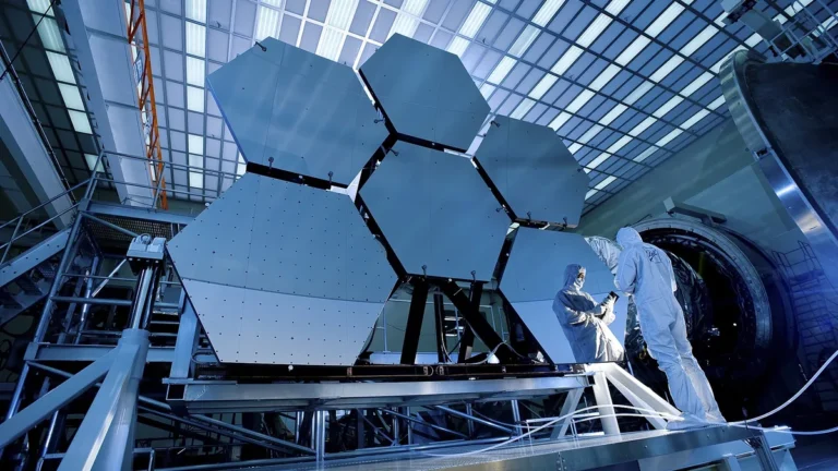 Technicians inspect giant hexagonal mirror segments of a next-generation space telescope in a cleanroom.