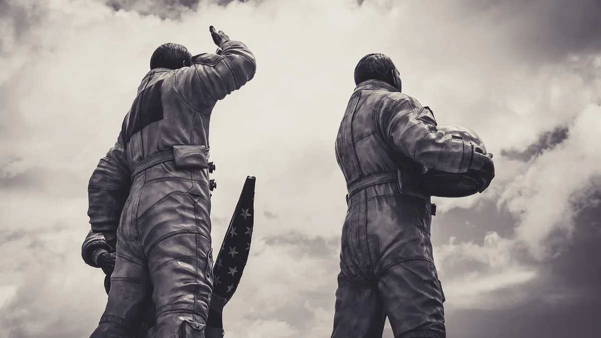 Statue of two astronauts in spacesuits looking towards the clouds, one saluting, one holding a helmet.