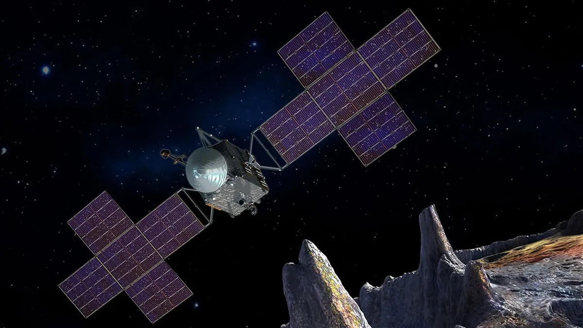 Artist concept of the Psyche spacecraft with large solar panels flying over a metallic asteroid in deep space.