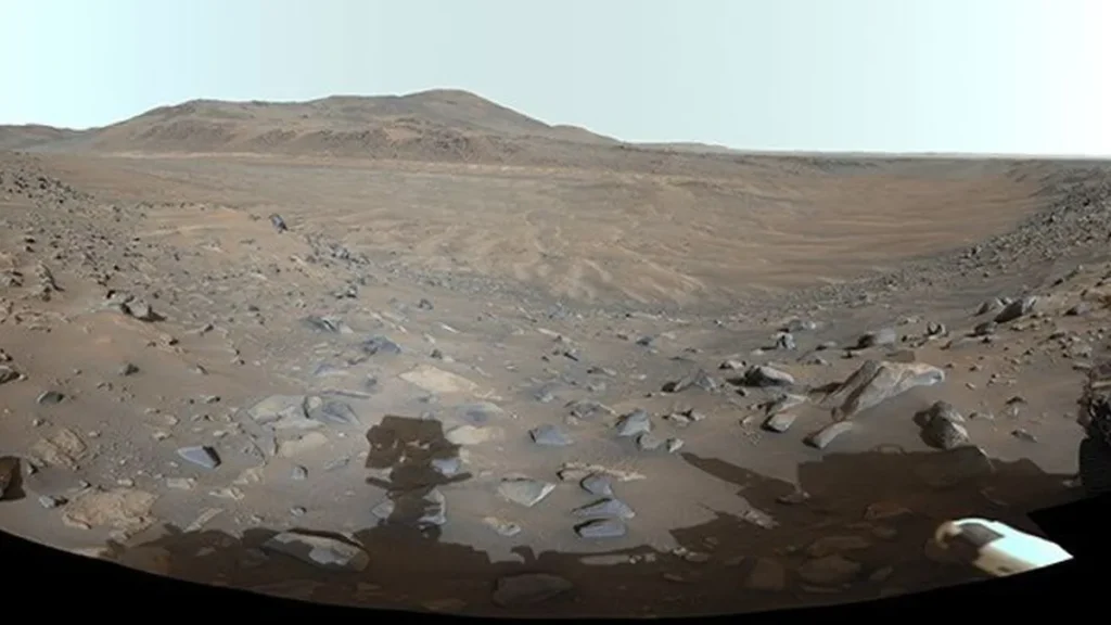 Wide panoramic view of a rocky Martian river valley under a pale sky, captured by NASA's Perseverance rover.