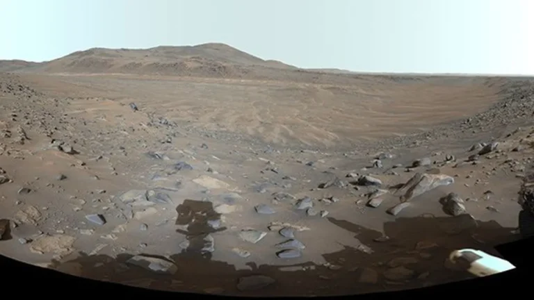 Wide panoramic view of a rocky Martian river valley under a pale sky, captured by NASA's Perseverance rover.