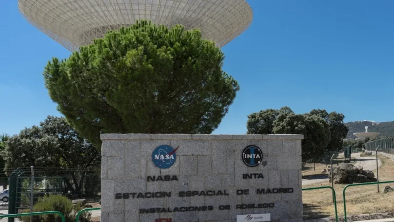 NASA and INTA sign at Madrid Space Station Robledo facility, with a giant satellite dish behind a tree.