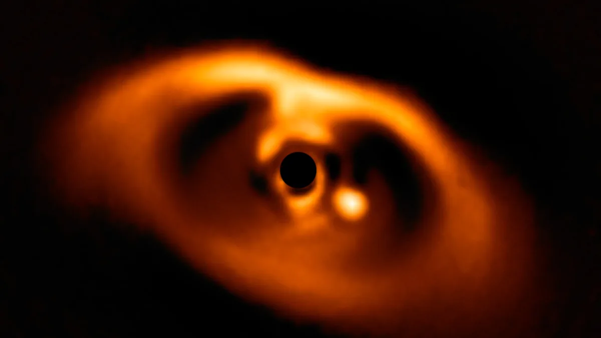 Orange glowing dusty disk with a central black circle masking the star and a bright planet forming nearby.