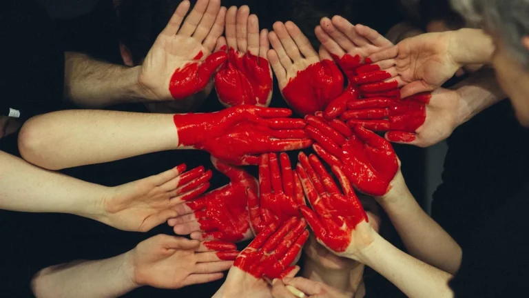 A circle of human hands, some painted bright red, coming together in unity and collaboration.
