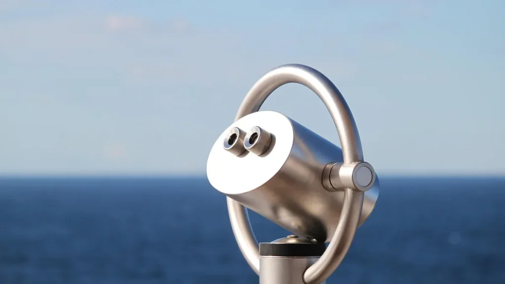A silver coin-operated telescope viewer overlooking a blue sea and sky.
