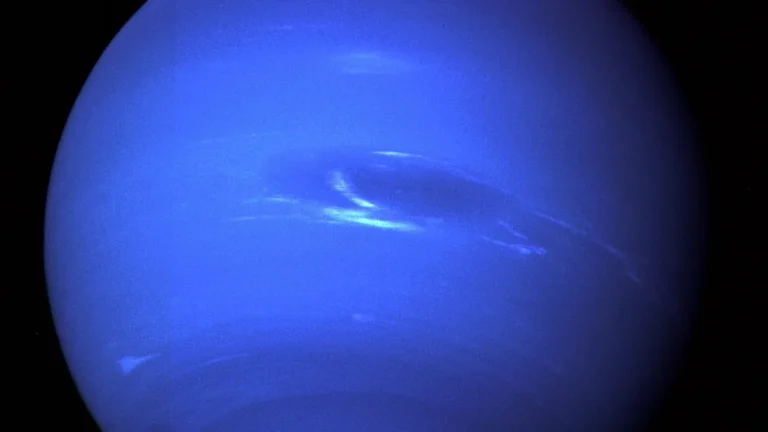 Vibrant blue planet Neptune showing swirling white clouds and a giant dark storm spot against black space.