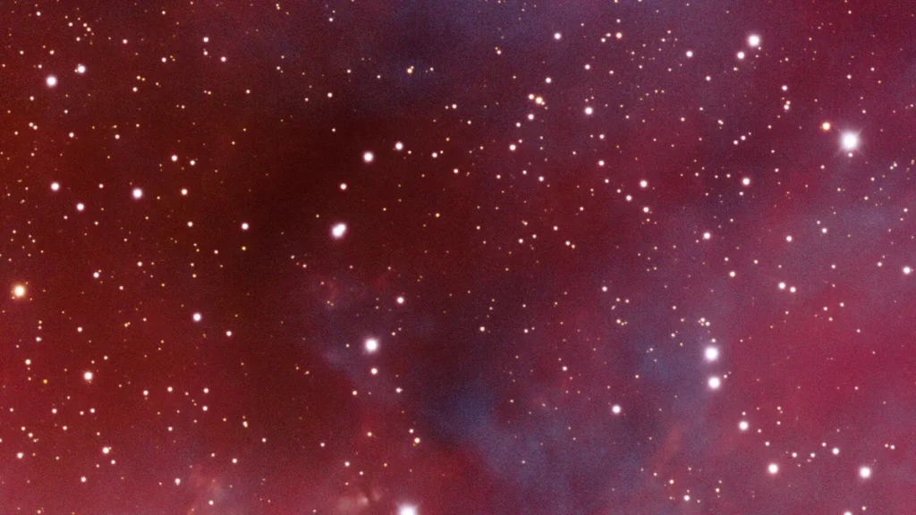 A vibrant star field glowing with red and purple nebula clouds, representing the vastness of interstellar space.