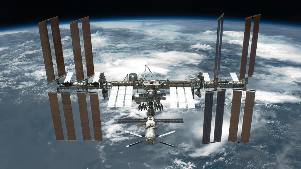 The International Space Station orbits Earth, displaying large solar arrays against the blue planet's curve.