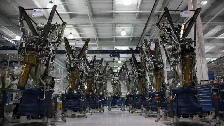 A row of SpaceX Merlin rocket engines lined up inside a manufacturing facility under blue protective covers.